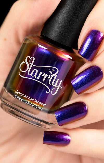 Raven (Multichrome) by Starrily, multichrome with vivid violet-to-blue-to-red-gold duochrome flare across nails and bottle, bottle held in a light skin tone hand