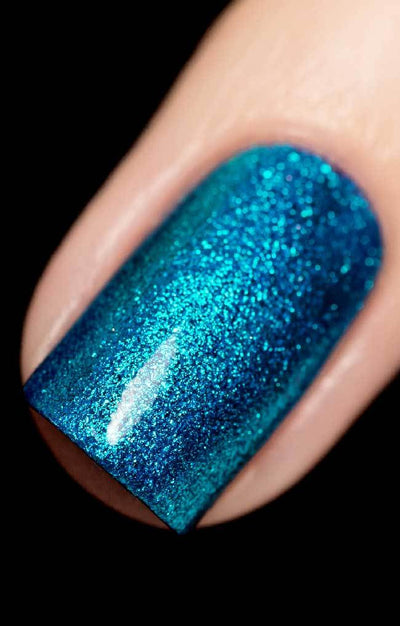 Skyline (Blue Foil) by Starrily, deep teal-blue reflective micro flakies with brilliant cyan foil flash under direct flash, on a light skin tone hand