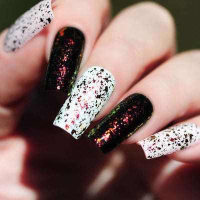Crunchy Leaves by Starrily, gold-green multichrome flakie topper layered over alternating black and white bases, orange-red-to-green flake shift in bright daylight, on a light skin tone hand