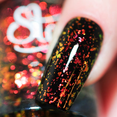Crunchy Leaves by Starrily, gold-green multichrome flakie topper with densely scattered red-orange to golden-amber flakes over black base, on a light skin tone hand