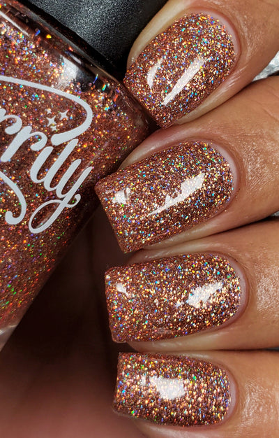 Penny by Starrily, copper holographic glitter in clear base with vivid rainbow scatter under direct flash, on a medium skin tone hand