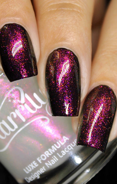 Zephirine by Starrily, color-shifting holographic shimmer topper with vivid pink-to-copper-orange shift over a deep blackened plum base, on a light skin tone hand