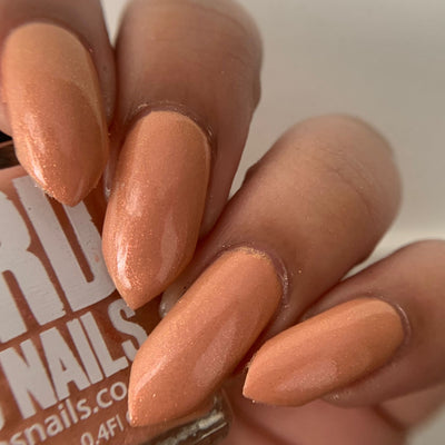 Winter Coat by 'Ard As Nails, warm peach-coral with fine golden-pink pearl shimmer under indoor warm lighting, on a medium skin tone hand
