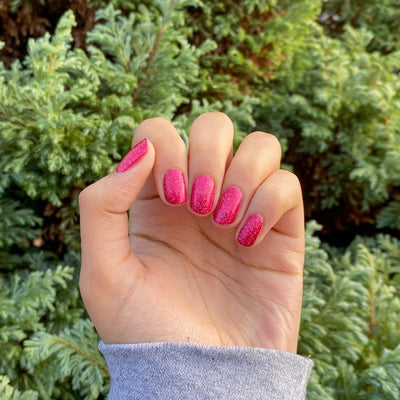 Party Dress by 'Ard As Nails, raspberry red foil base with scattered hot pink holographic flakies, vivid foil shimmer in bright daylight, on a light-medium skin tone hand