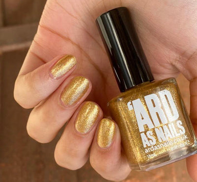 Christmas Cracker by 'Ard As Nails, warm antique gold foil with metallic shimmer, bottle held in a light hand