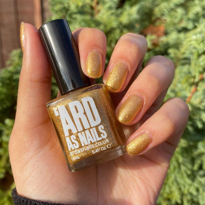 Christmas Cracker by 'Ard As Nails, bright amber-gold foil with intense metallic sparkle in daylight, bottle held in a light-medium hand