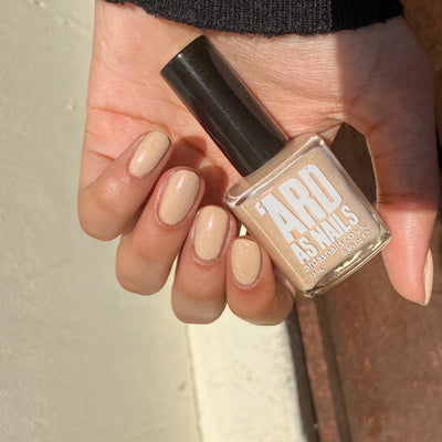 Warm Fleece by 'Ard As Nails, warm sandy beige cream base with golden pink shimmer, bottle held in a light-medium skin tone hand