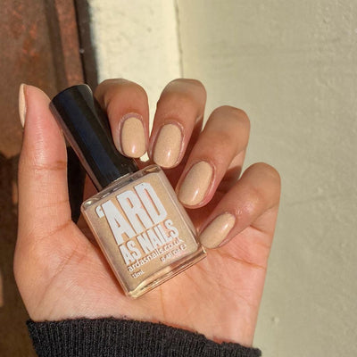 Warm Fleece by 'Ard As Nails, warm sandy beige cream with pink-gold micro-shimmer, bottle held in a medium skin tone hand