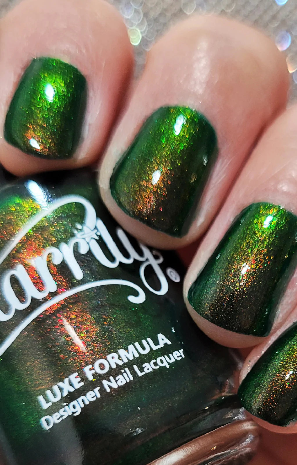 Artemis by Starrily, forest green shimmer reading bright olive-green in direct light and burnt copper in shadow, indoor warm lighting, on a light skin tone hand