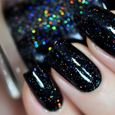 Neutrino by Starrily, jet black holographic glitter refracting into vivid blue, orange, green, and red spectral points under direct flash, on a light skin tone hand