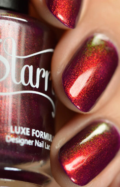 Dragon by Starrily, deep burgundy-purple base with copper-red to green color-shifting shimmer in bright daylight, bottle held in a light-medium hand