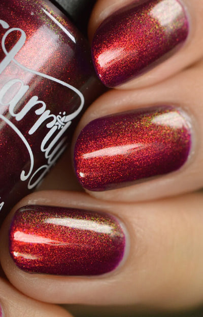 Dragon by Starrily, deep burgundy-plum base with copper-red shimmer in direct light and gold-green shift at angles, on a light-medium skin tone hand
