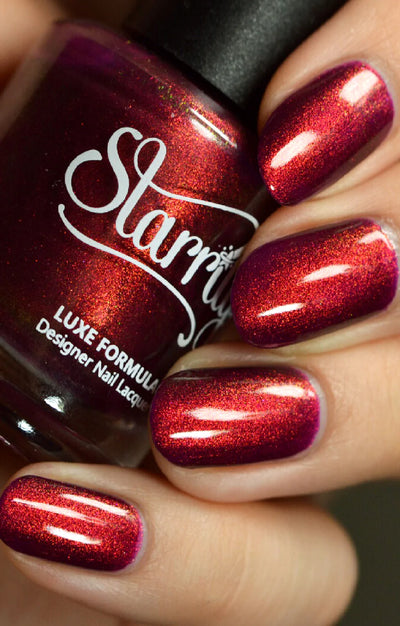 Dragon by Starrily, deep berry-purple base shifting to vivid copper-red in direct light with color-shifting shimmer particles, bottle held in a light-medium hand