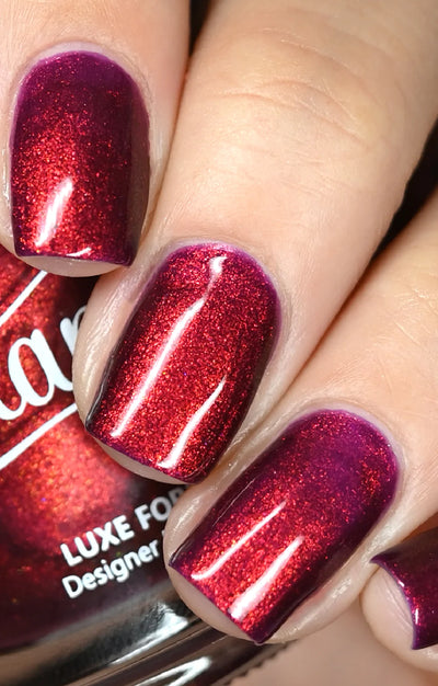 Dragon by Starrily, deep magenta-purple base shifting to bright copper-red under direct flash, on a light skin tone hand