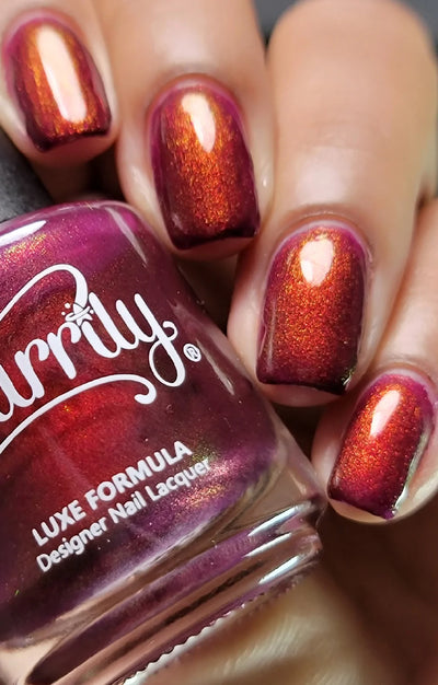 Dragon by Starrily, deep magenta-purple base with copper-orange shimmer shift in warm indoor light, bottle held in a light-medium hand