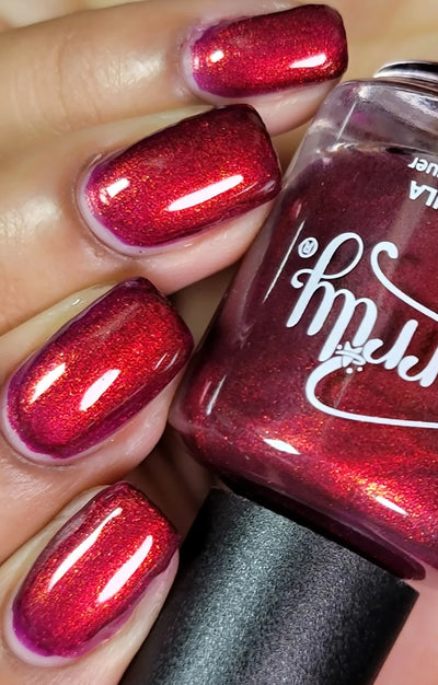 Dragon by Starrily, deep crimson-burgundy base with copper-orange shimmer flash activated by direct flash, on a light-medium skin tone hand