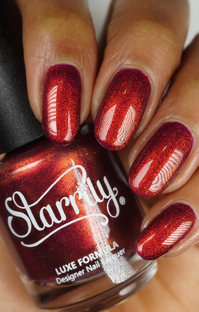 Dragon by Starrily, deep burgundy-purple base blazing copper-red in bright daylight, bottle held in a medium hand