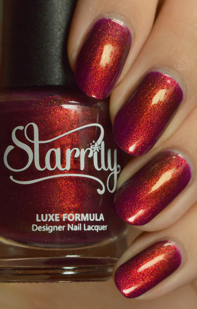 Dragon by Starrily, deep magenta-purple base with dramatic copper-red shimmer shift in studio light, bottle held in a light hand
