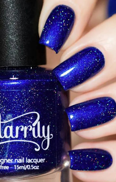 Heart of the Ocean by Starrily, deep sapphire blue holographic with scattered electric-blue and multicolor micro-flake shimmer, bottle held in a light skin tone hand