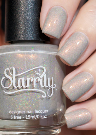 Moon Glow by Starrily, grey holographic shimmer creme showing soft copper shimmer and scattered micro holographic flecks in warm indoor light, bottle held in a light hand