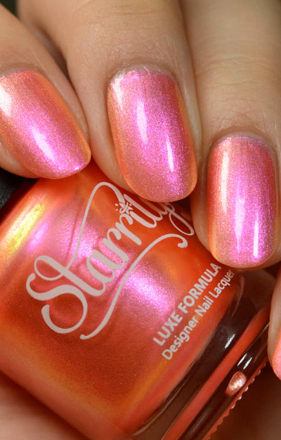 Moon Sugar by Starrily, coral-orange shimmer with strong pink-to-gold color-shifting shimmer in bright daylight, on a light skin tone hand