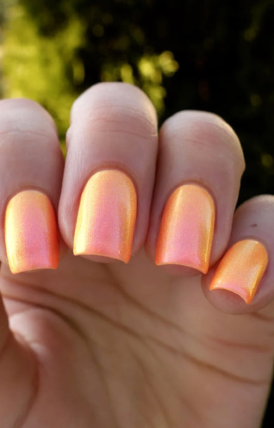 Moon Sugar by Starrily, warm orange multichrome shimmer with golden yellow-orange and coral-pink shift in bright outdoor daylight, on a light skin tone hand