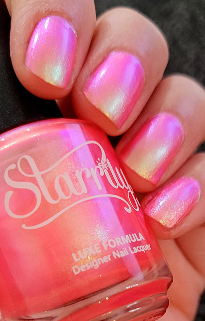 Nectar by Starrily, hot coral-pink multichrome shimmer revealing pink-to-green pearly shift under direct flash, bottle held in a light hand