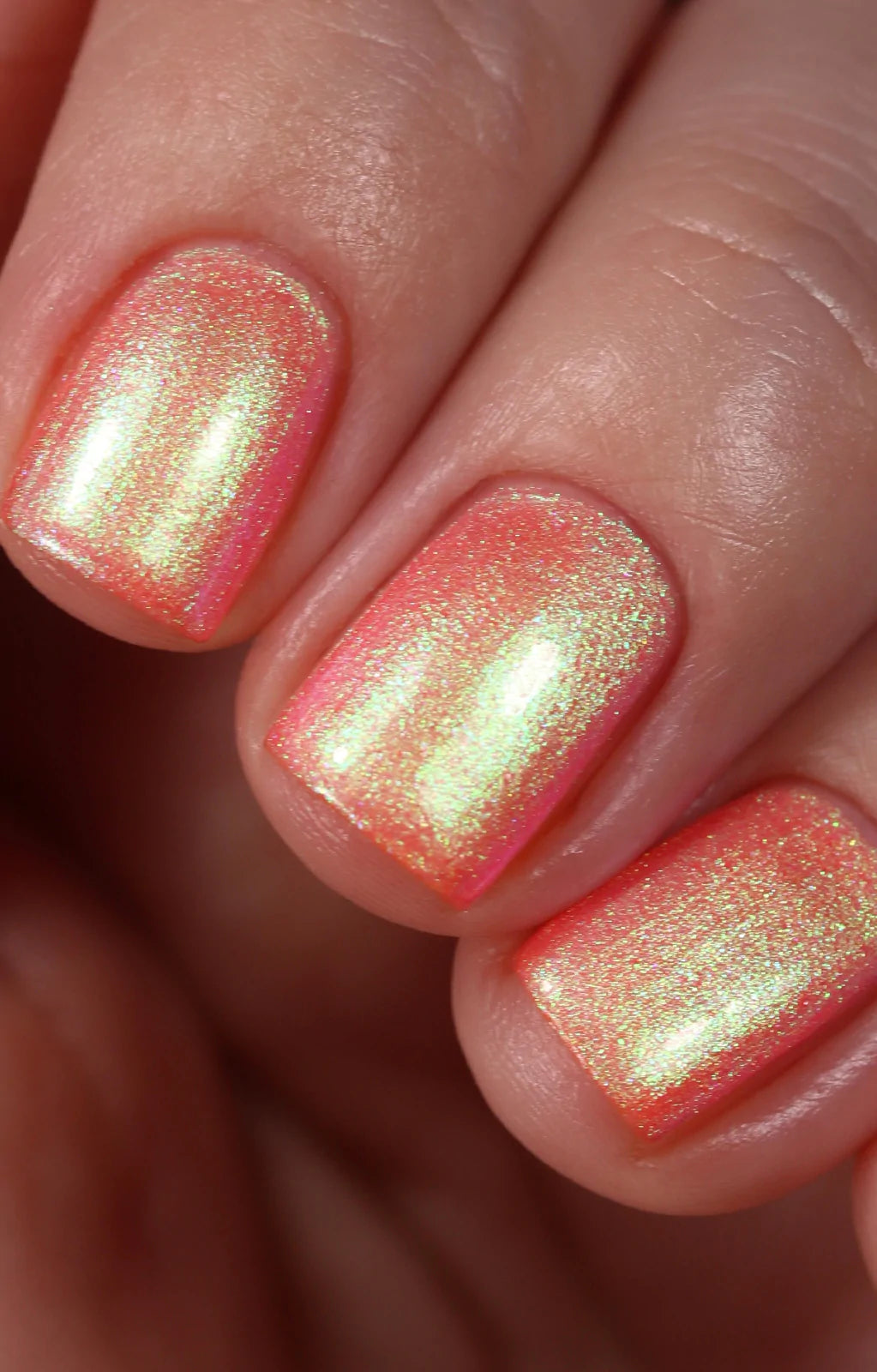 Nectar by Starrily, coral-pink base with intense yellow-green duochrome shimmer shift and fine metallic particles, on a light skin tone hand