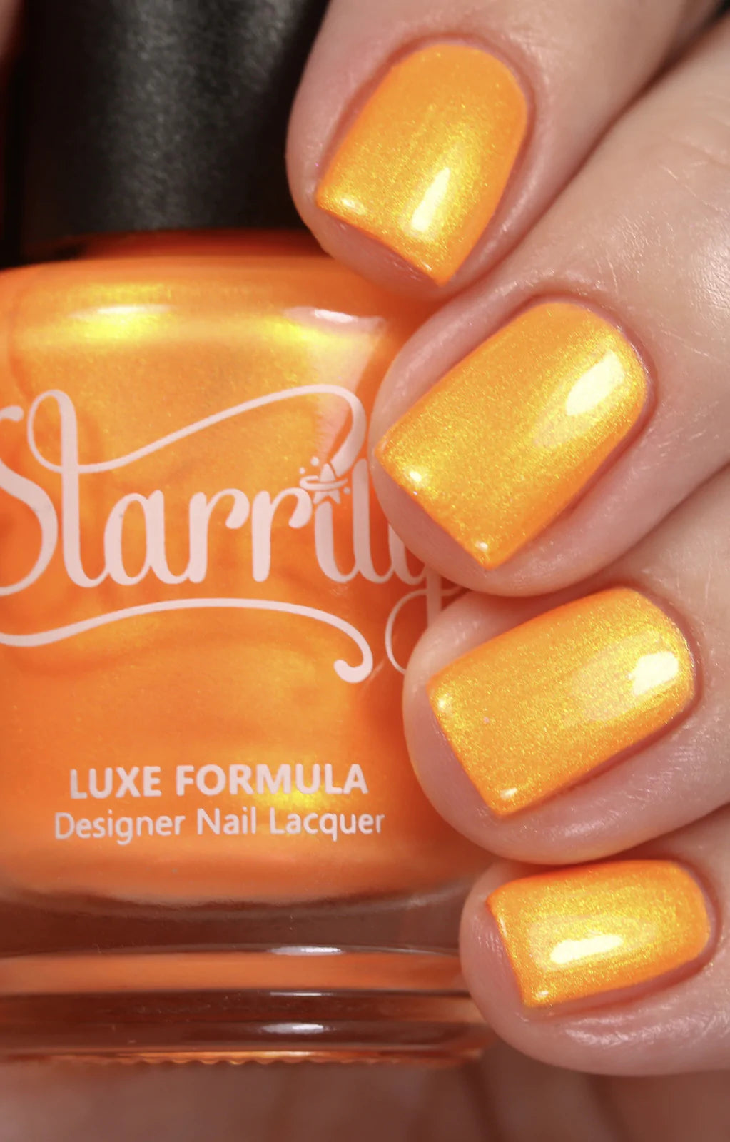 Peach Glow by Starrily, vivid orange base with gold and green color-shifting shimmer in studio light, bottle held in a light hand