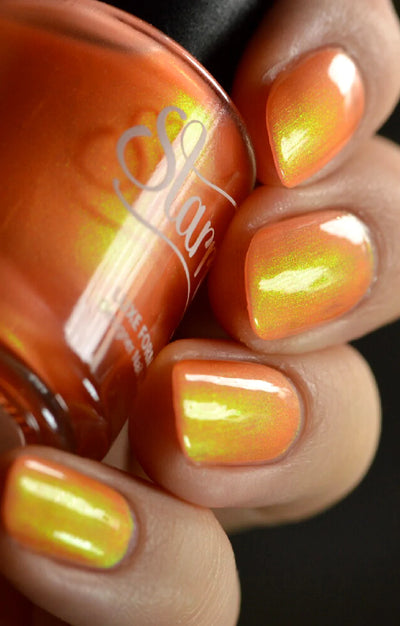 Peach Glow by Starrily, warm orange base with intense yellow-green to gold shimmer shift in studio light, bottle held in a light hand