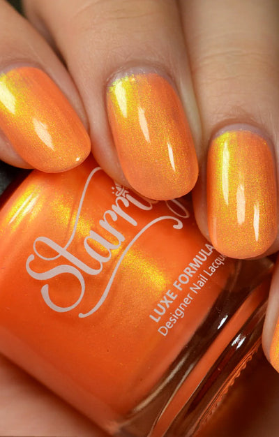 Peach Glow by Starrily, warm coral-orange base with gold-to-yellow-green shimmer flash in daylight, bottle held in a light hand