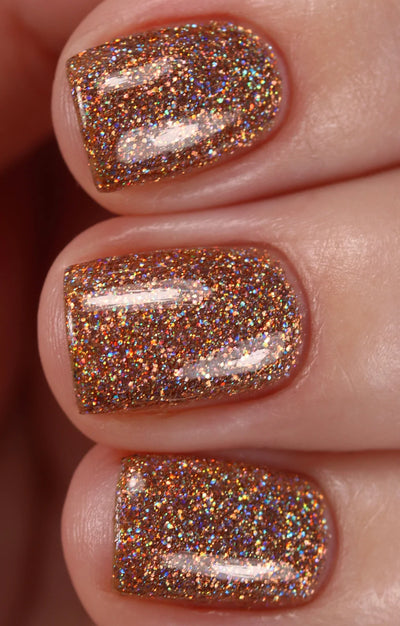 Penny by Starrily, copper and golden-orange holographic micro glitter with scattered rainbow sparkle in bright daylight, on a light skin tone hand