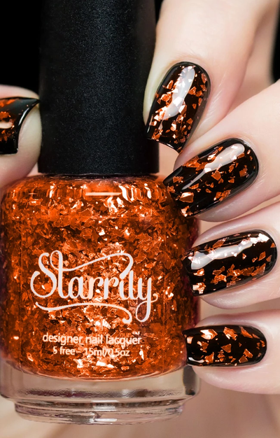 Citrine by Starrily, clear-base orange glitter topper with large irregular copper-orange shard flakies, bottle held in a light skin tone hand