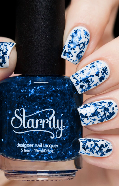 Lapis Lazuli by Starrily, navy and metallic blue flake glitter topper in clear base over white creme, layering demo on a light skin tone hand