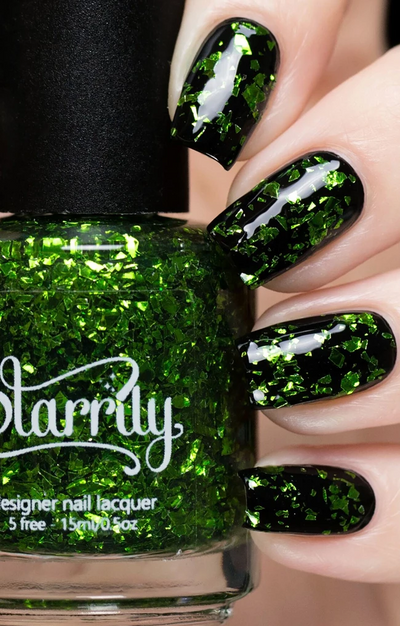 Peridot by Starrily, green glitter topper with large vivid foil flakes in a clear base, layered over black creme, bottle held in a light skin tone hand