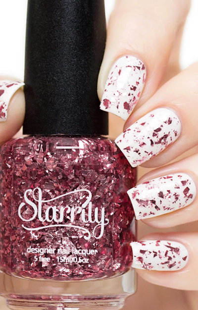 Rose Quartz by Starrily, deep rose-pink metallic flake glitter topper in clear base, with large shimmering flake pieces, bottle held in a light skin tone hand