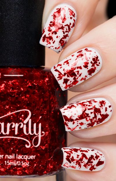 Ruby by Starrily, red metallic flakie glitter topper with large reflective foil shards over white creme, on a light skin tone hand