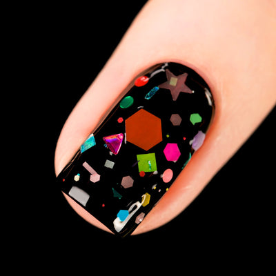 Toy Story by Starrily, chunky multicolor glitter topper over black base showing large rust-orange and hot pink hexagons with iridescent geometric shapes, on a light skin tone hand