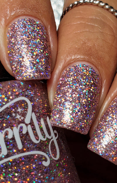 Dollhouse by Starrily, dusty mauve-pink holographic micro-glitter showing intense gold-orange holographic flash in bright daylight, on a medium-deep skin tone hand