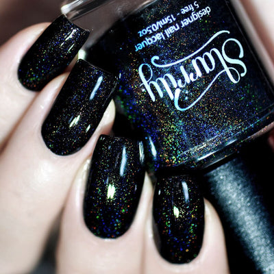 Black Magic by Starrily, jet black holographic glitter with intense gold, blue, and green rainbow scatter, on a light skin tone hand