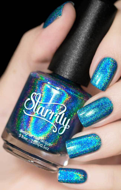 Cat Eyes by Starrily, medium blue holographic with teal and violet metallic shimmer scatter, bottle held in a light skin tone hand