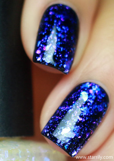 Patronus by Starrily, deep indigo-to-violet iridescent flakie topper with large ultrachrome shards over black, on a light skin tone hand