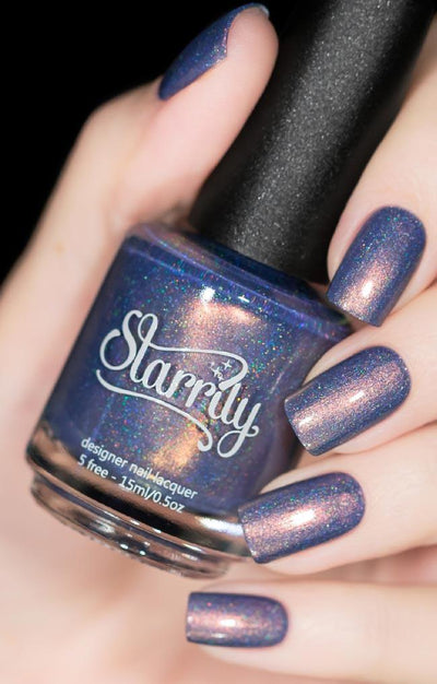 The Cat's Meow by Starrily, dusty blue-purple holographic shimmer creme with vivid copper flash and linear holo flecks, bottle held in a light skin tone hand