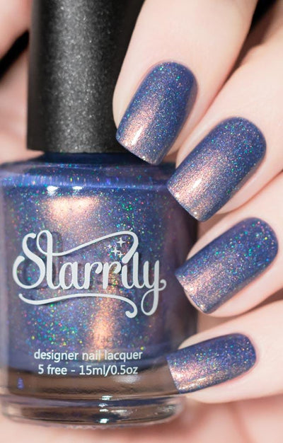 The Cat's Meow by Starrily, periwinkle-blue holographic shimmer creme showing soft violet shift with strong copper shimmer flash, bottle held in a light skin tone hand
