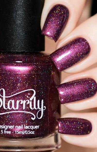 True Blood by Starrily, deep plum-maroon holographic with micro flakes flashing magenta and rainbow under studio light, bottle held in a light hand