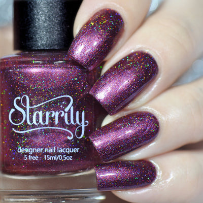 True Blood by Starrily, deep burgundy-plum holographic with scattered pink and red micro flecks catching studio light, bottle held in a light hand