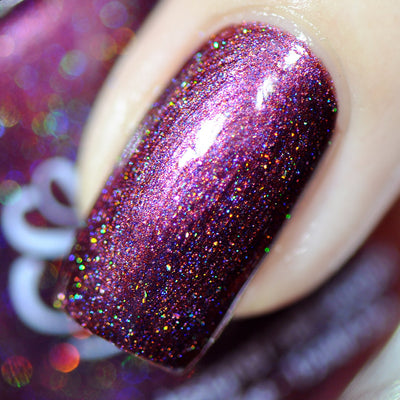 True Blood by Starrily, deep maroon-plum holographic showing vivid rainbow scatter with dense micro holo flakes under direct flash, on a light skin tone hand