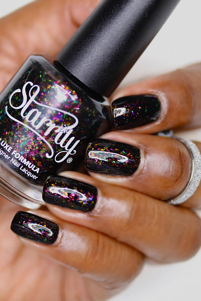 Planet X by Starrily, black flakie jelly with magenta-pink and green rainbow multichrome flakes, bottle held in a deep hand