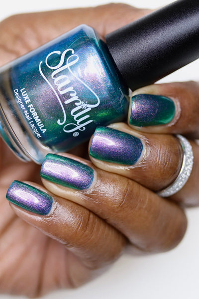 Sleepy Hollow by Starrily, teal green shimmer mid-shift from green to violet-pink with fine pearly shimmer particles, bottle held in a rich skin tone hand