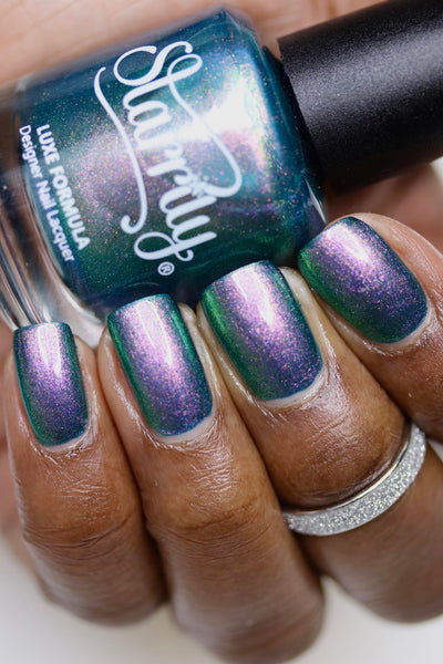Sleepy Hollow by Starrily, deep teal green shimmer with shifting pink-violet and green multichrome flash, bottle held in a deep skin tone hand